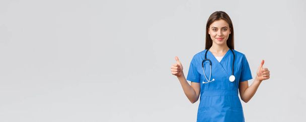 Медицинские работники, предотвратить вирус, страхование и медицина концепции. Поддерживающая профессиональная женщина-медсестра или врач в синей форме, стетоскоп, показать большой палец вверх в одобрении, улыбаясь
 - Фото, изображение