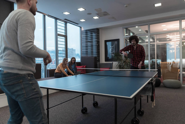 Двоє молодих бізнесменів, які грають в теніс пінг-понг в сучасному творчому офісному просторі, люди зустрічаються і мозковий штурм на задньому плані
 - Фото, зображення