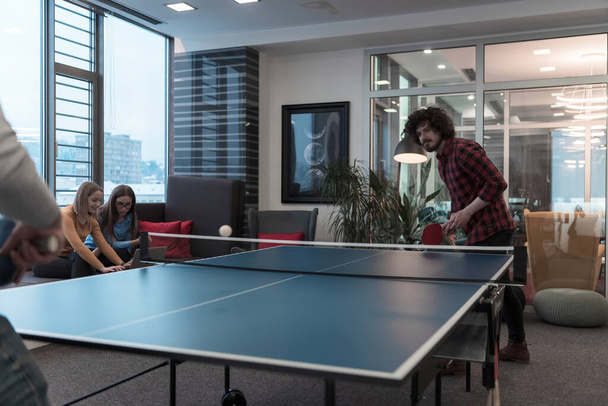 Двоє молодих бізнесменів, які грають в теніс пінг-понг в сучасному творчому офісному просторі, люди зустрічаються і мозковий штурм на задньому плані
 - Фото, зображення