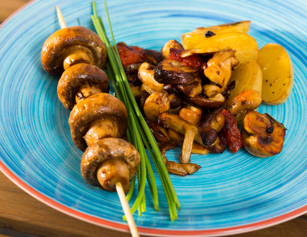 Tasty different mushrooms frying with potatoes at plate at table - Foto, Imagen