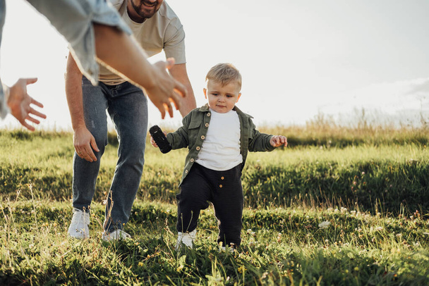 Father and Mother Help Their Toddler Son Take the First Steps, Family Weekend Outdoors - Foto, imagen