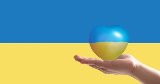 Hand hält Herz mit Druck der ukrainischen Nationalflagge in den Händen, Kopierraum. Schluss mit Krieg und Frieden in der Ukraine, Freiheit für die Ukraine, Hände hoch - Foto, Bild