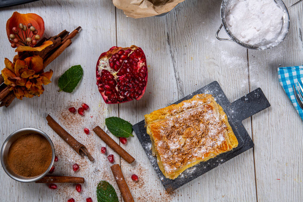 Traditional Turkish Boregi with almonds, sprinkled with powdered sugar, made on a tray. Table presentation garnished with pomegranate and cinnamon. food photography - Foto, imagen