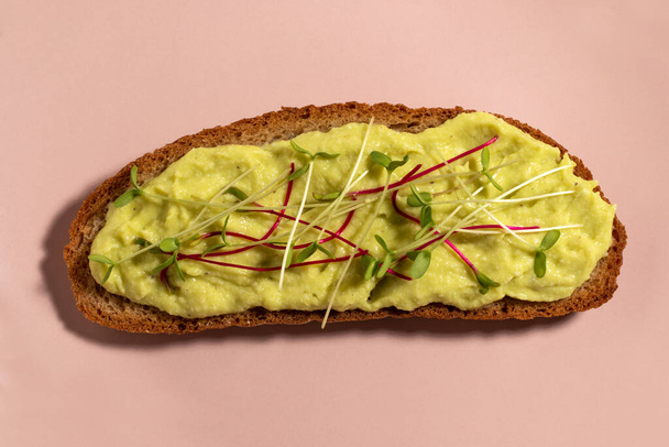 A slice of bread smeared with avocado mash and seasoned with microgreens. Avocado sandwich. - Фото, изображение