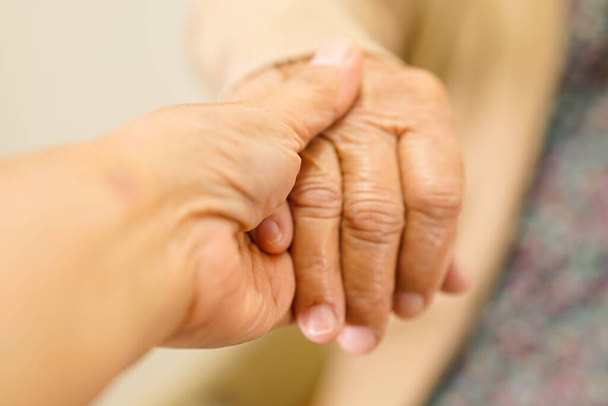Опекун держит за руки азиатскую пожилую женщину пациент, помощь и уход в больнице.        - Фото, изображение