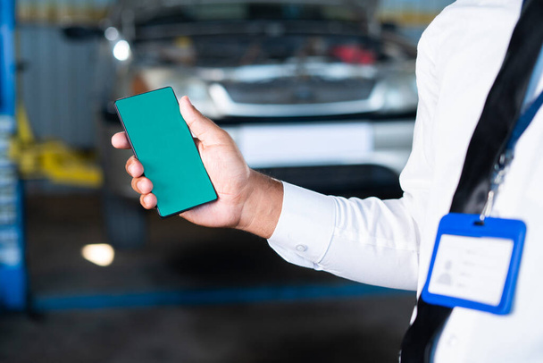 Lähikuva laukaus kädet vihreällä näytöllä matkapuhelin edessä rikki auton autotallissa käsite mainos korjauspalvelu, sovelluksen edistäminen ja teknologian - Valokuva, kuva