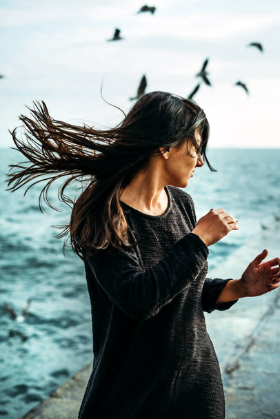 Eine Frau steht am Meer und der Wind bläst ihr die Haare, im Hintergrund Möwen. Urgewalt. - Foto, Bild