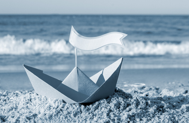 Sininen paperivene hiekkarannalla lähellä merta aurinkoisena kesäpäivänä. - Valokuva, kuva