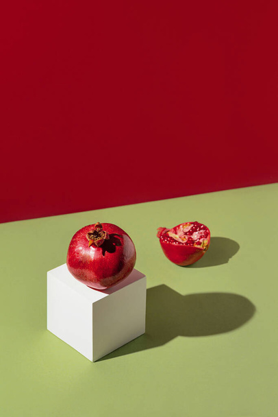 Creative composition made of fresh pomegranates on green and red background with white cube and shadows. Minimal style. Refreshment concept. Healthy food ingredient theme. - Foto, Imagen