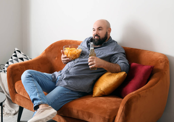 Ленивый человек пьет пиво и ест чипсы дома - Фото, изображение