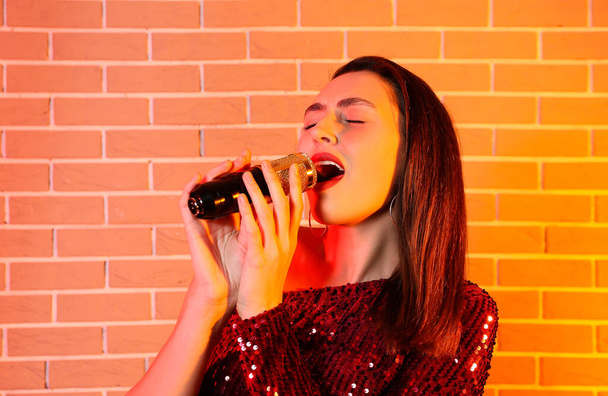 Pretty young singing woman with microphone on color brick background - Fotó, kép
