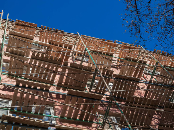 Metallgerüste mit hölzernen Trennwänden stehen neben einem Backsteingebäude. Ansicht von unten. Gebäudesanierung. - Foto, Bild