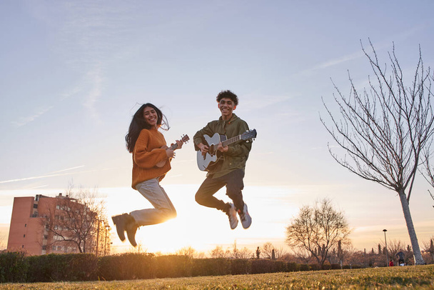 Happy young man and young woman jumping with guitar and ukulele over blue sky - Photo, Image