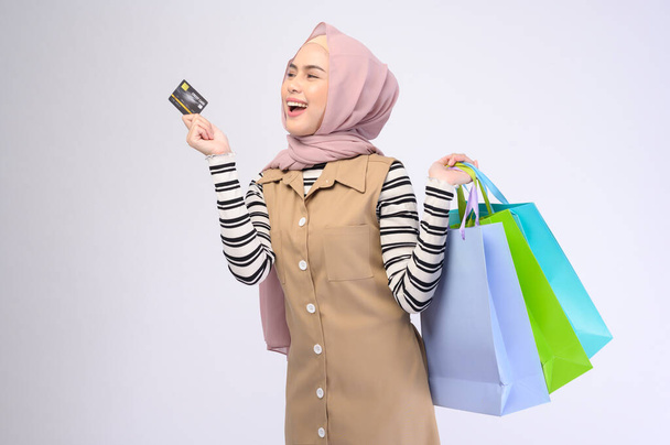 A young beautiful muslim woman in suit holding colorful shopping bags over white background studio - Photo, image