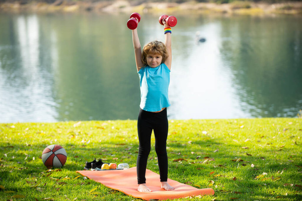 Sport children. Kids exercising fitness dumbbells. Strong little boy exercising with dumbbell in park outdoor. - Photo, image