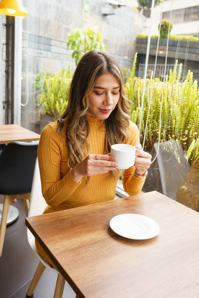 krásná žena s dlouhými blond vlasy a make-up sedí čeká v kavárně interiéru, těší lahodný šálek kávy, ranní nápoj - Fotografie, Obrázek