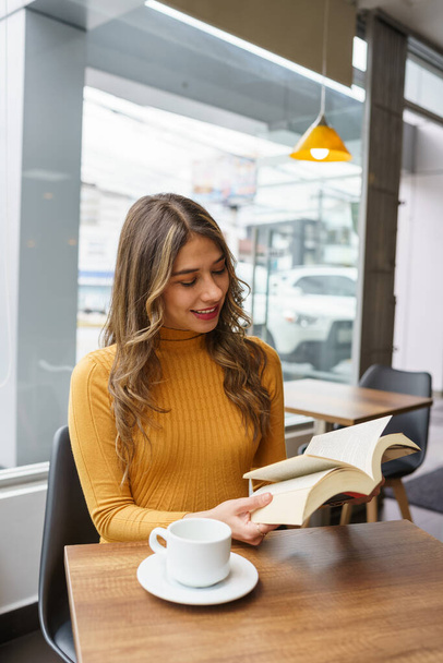 Lebensstil einer jungen lateinischen Frau mit langen blonden Haaren, die es genießt, ein Buch zu lesen, auf dem Tisch eine Tasse Kaffee, Wissen und Lernen - Foto, Bild