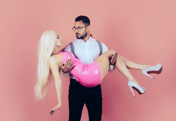 Handsome elegant young man holding his girlfriend in his arms. Funny Valentines day. Fun couple on pink isolated background. Funny man holds and hug woman in arms. Sexy couple. - Foto, imagen