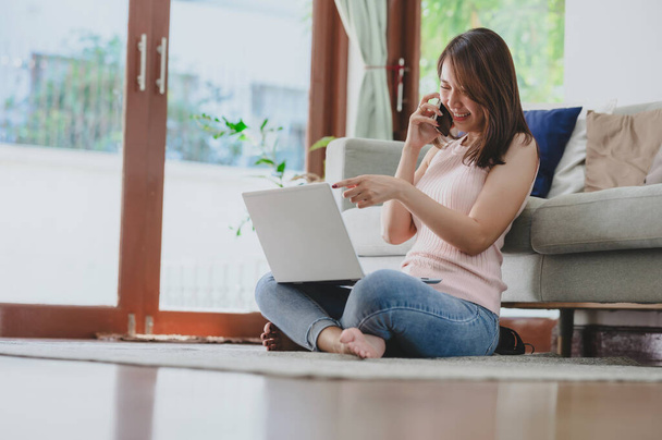Boldog ázsiai nő nevet, miközben beszél az okostelefon és a laptop használata otthon - Fotó, kép