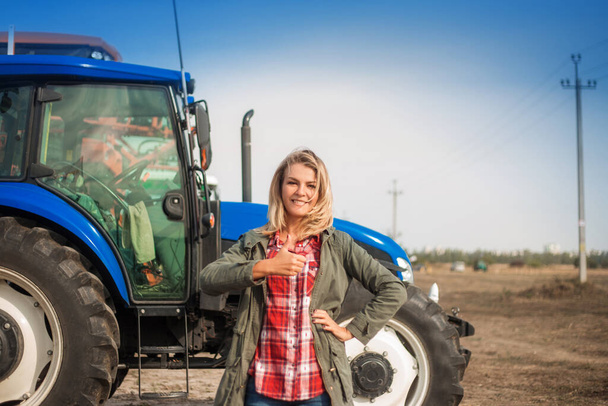 Jolie femme souriante avec des émotions positives sur le fond d'un tracteur dans un champ. - Photo, image