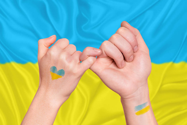 Two arms with crossed fingers symbolizing peace glory to Ukrainian savers couple lovers reunion after war finishing in front of national colors flag - Foto, immagini