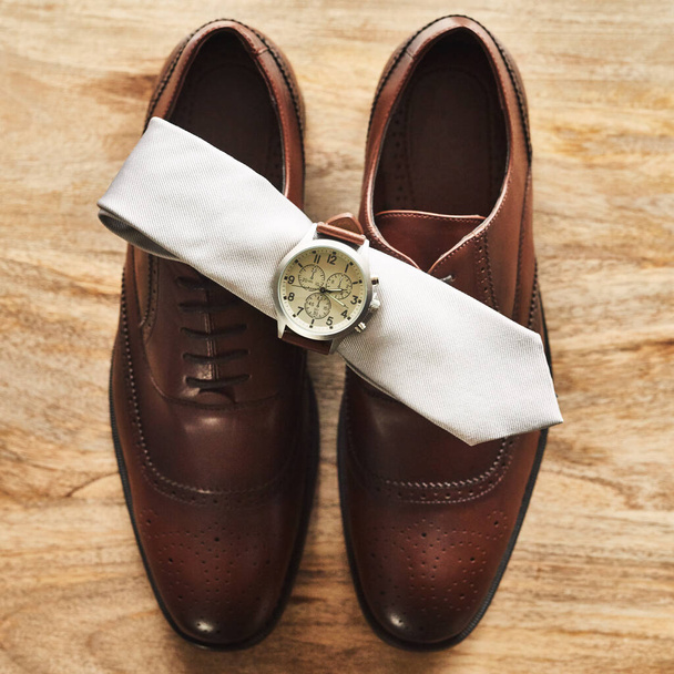 Classic never goes out of fashion. Still life shot of a wristwatch and tie on top of formal shoes on a wooden surface. - Фото, изображение