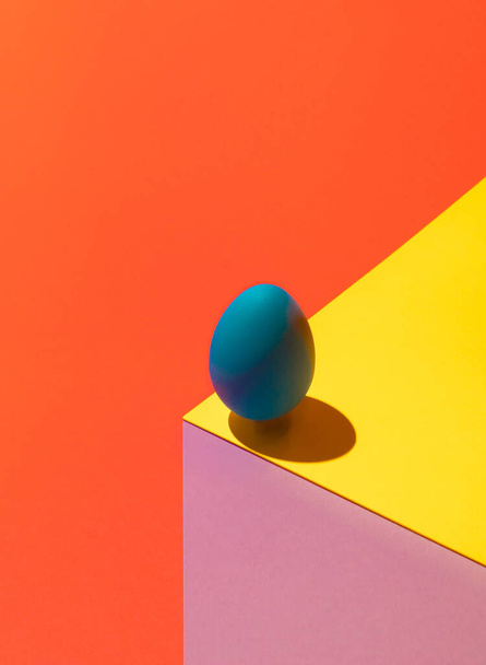 Nowoczesna iluzja optyczna wykonana z pisanki na kolorowym tle. 3D renderować niebieskie jajko na kostce papieru. Abstrakcyjny skład wielkanocny. - Zdjęcie, obraz