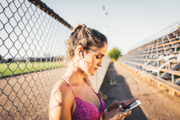 Beautiful caucasian young active woman setting a music playlist on her smartphone before start running. - Φωτογραφία, εικόνα