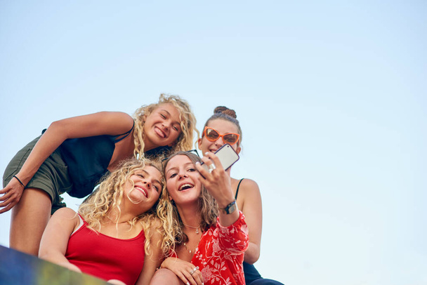 Its all about the angle. Low angle shot of a group of attractive young girlfriends taking selfies in the city. - Fotografie, Obrázek