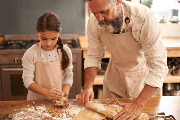Ze zijn serieus over het bakken. Shot van een meisje en haar grootvader bakken samen in de keuken. - Foto, afbeelding