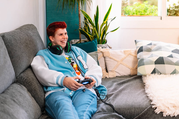 Niet-binaire lachende persoon die videospelletjes speelt in de woonkamer thuis - Foto, afbeelding