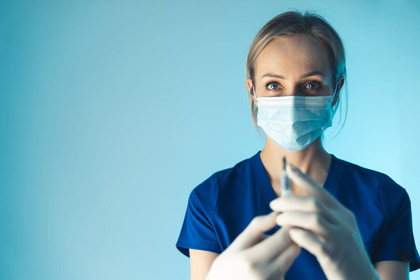 Jovem médica caucasiana preparando injeção de antibiótico. Médio close-up estúdio tiro fundo azul. - Foto, Imagem