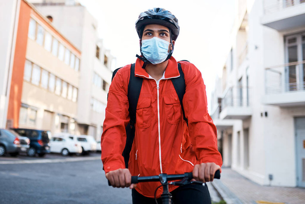 Masked and ready for his next delivery. Shot of a masked man out on his bicycle to do a delivery. - 写真・画像