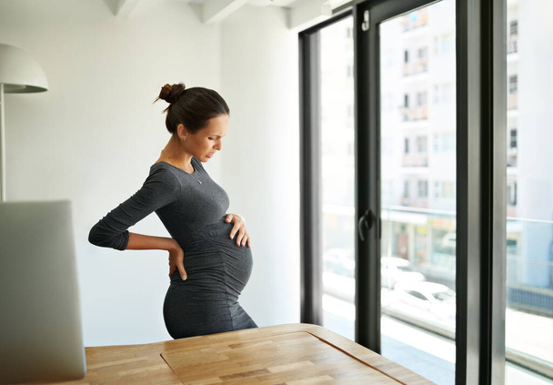 Any day now.... Shot of a pregnant businesswoman standing in her office holding her stomach. - Foto, Bild