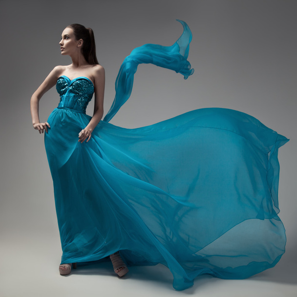 Fashion woman in fluttering blue dress. Gray background. - Photo, image