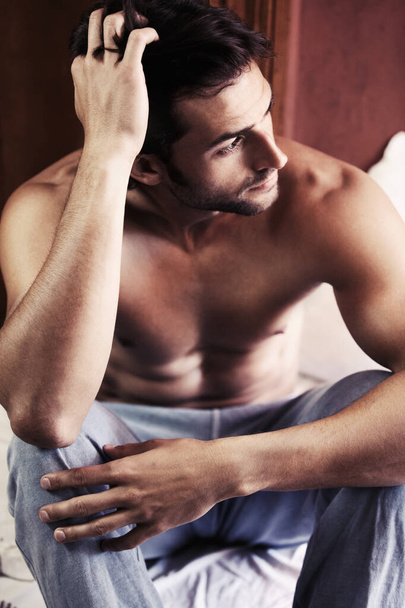Contemplating his future decisions. Sexy young man sitting on the edge of his bed deep in thought. - 写真・画像