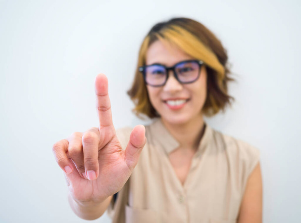 Closeup finger touch on virtual touch screen by happy smile Asian woman short hair wearing eye glasses with blue filter on white background. Hand point or press on empty space by businesswoman's hand. - Photo, Image