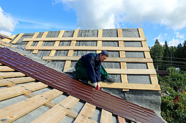 Працівник кладе металеву плитку на дах дерев'яного будинку
 - Фото, зображення