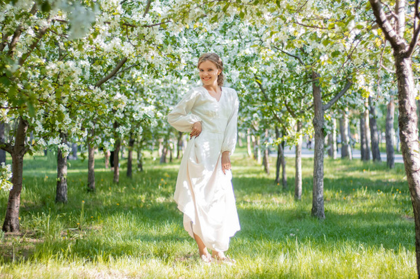Jeune femme en robe blanche sur fond de pommiers en fleurs. La fille pose sur le fond de fleurs dans le parc du printemps. - Photo, image