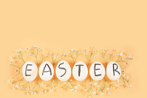 Білі яйця з чорними літерами EASTER навколо квітів гіпсофіли на жовтому фоні
. - Фото, зображення