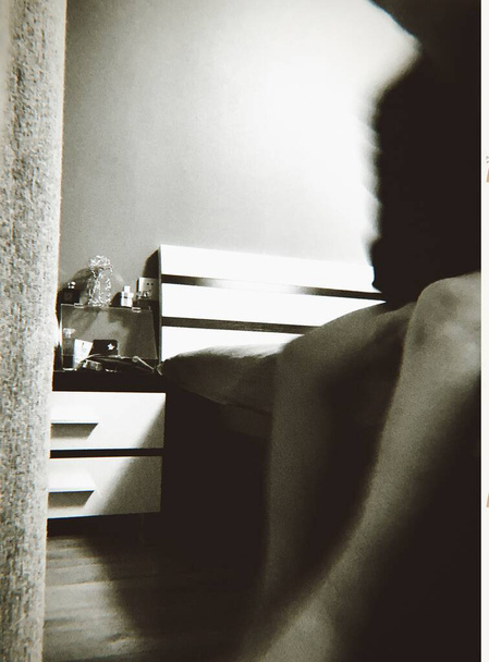 black and white photo of a young woman sitting on the bed and looking at the window - Fotó, kép