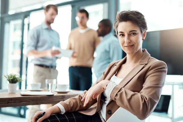 Here to become the best in the industry. Portrait of a young businesswoman sitting in an office with her colleagues in the background. - Фото, изображение