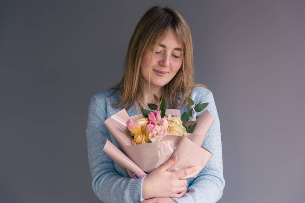 Portrait of a young woman with a bouquet of roses on a gray background. - Photo, Image