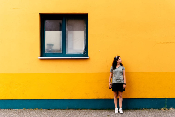 Mujer joven apoyada en una pared de wellow brillante - Foto, Imagen