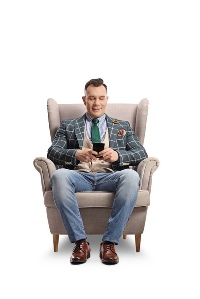 Fashionable man sitting in an armchair and using a smartphone isolated on white background - Photo, Image