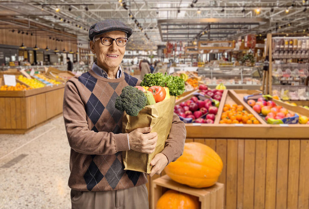 Elderly male customer in a grocery store with a paper bag standing in front of fruit shelves - Photo, image