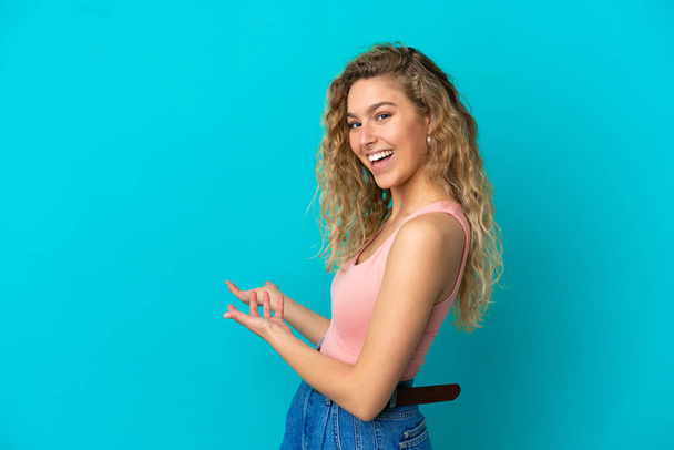 Young blonde woman isolated on blue background extending hands to the side for inviting to come - Foto, immagini