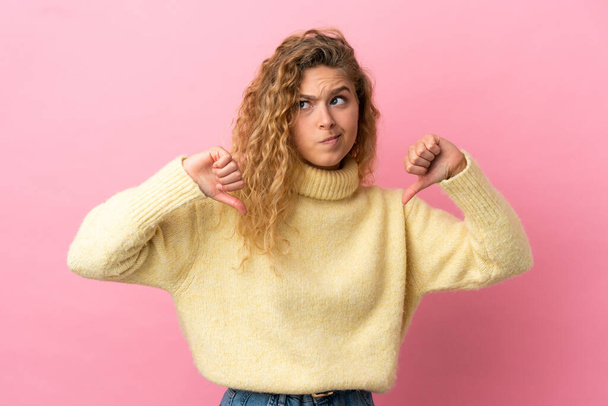 Young blonde woman isolated on pink background showing thumb down with two hands - Photo, Image