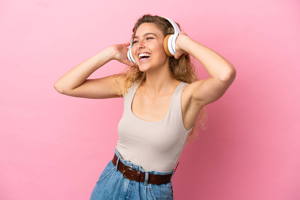 jong blond vrouw geïsoleerd op roze achtergrond luisteren muziek - Foto, afbeelding