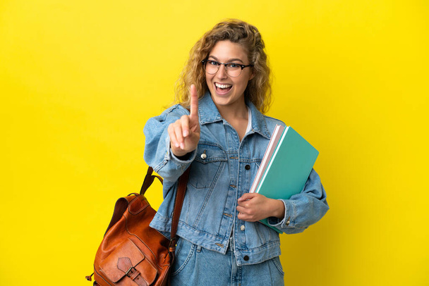 Молода студентка біла жінка ізольована на жовтому тлі, показуючи і піднімаючи палець
 - Фото, зображення